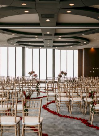 A large conference room with rows of chairs facing a panel at the front, beige walls, and a long table under a ceiling fan.