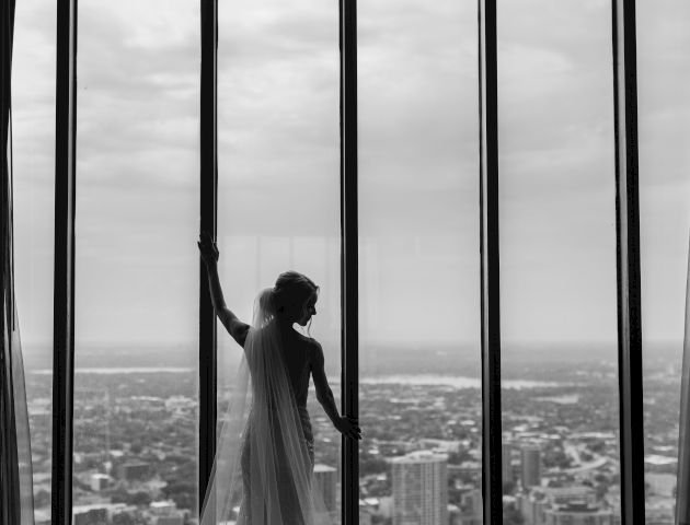 A person stands on a rocky shore, looking toward the sea under a cloudy sky, with dark vertical posts in the foreground.