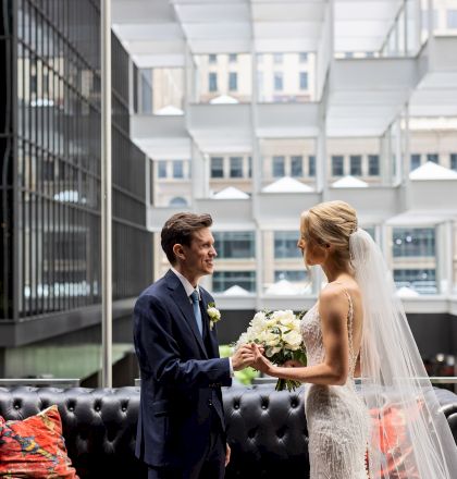 A person sits on a bench inside a modern train station or airport concourse, with a large window and bright, airy interior behind.