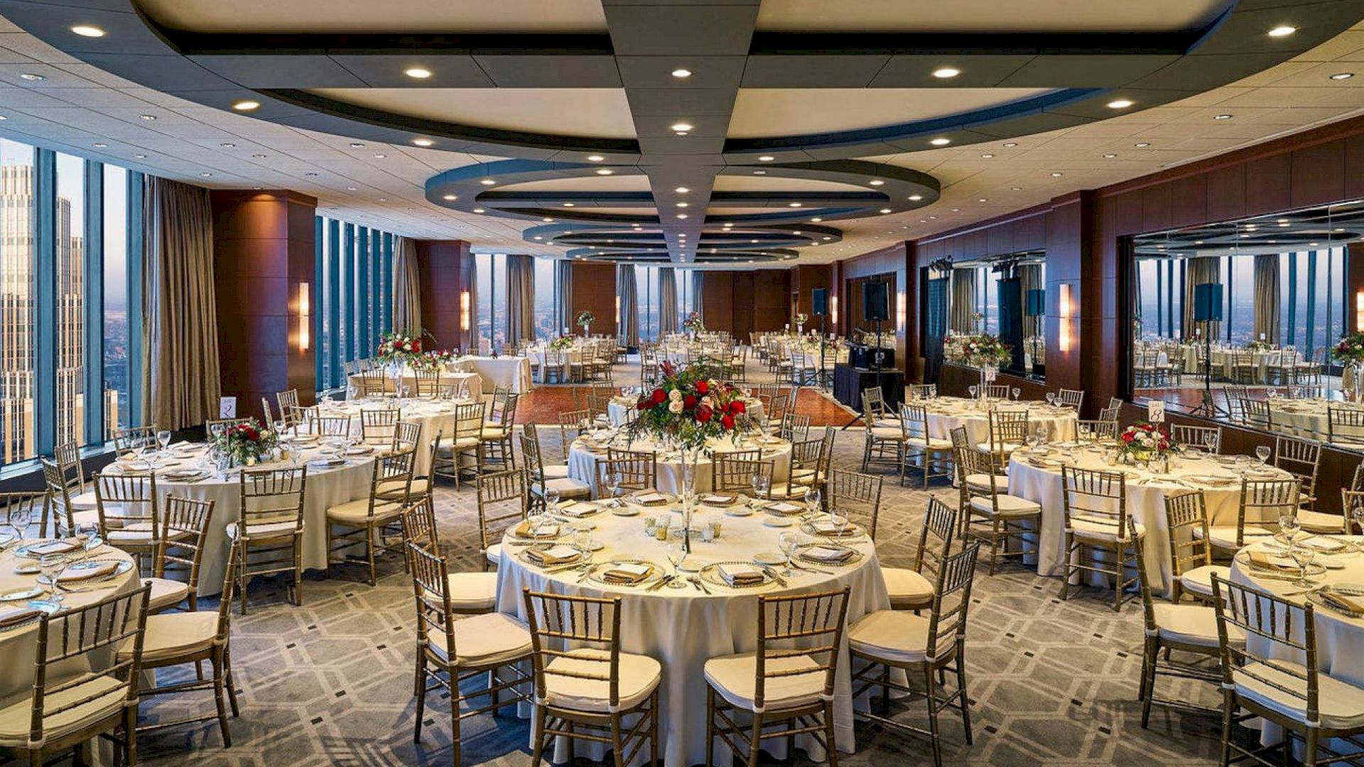 A formal banquet hall with round tables, elegant place settings, and floral centerpieces, set for a large reception or dinner.