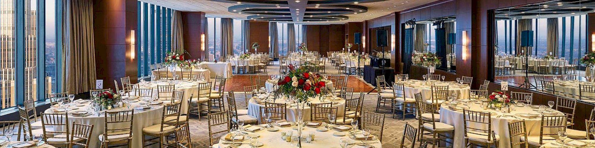 A formal banquet hall with round tables, elegant place settings, and floral centerpieces, set for a large reception or dinner.