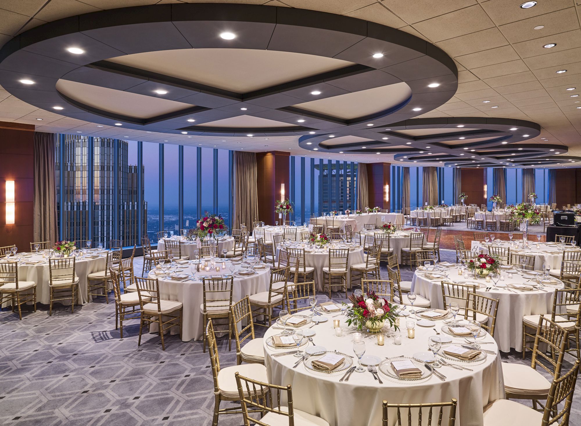 Elegant banquet hall with round tables, white linens, floral centerpieces, and warm lighting, ready for a formal event.