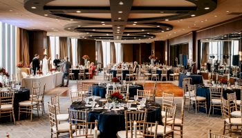 A formal conference or banquet setup with round tables, chairs, and a podium in a spacious, well-lit hall. event seating ready for attendees.