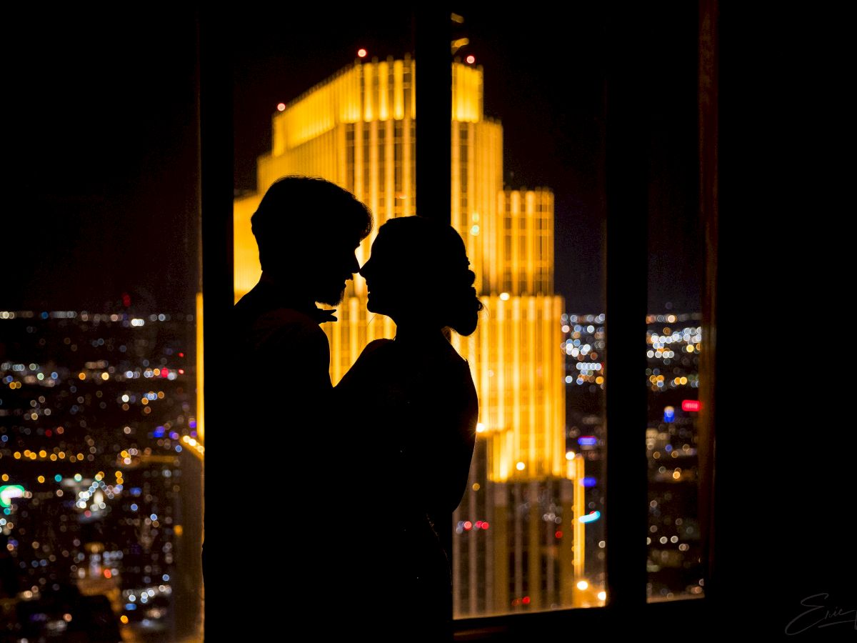 A silhouetted couple kissing against a nighttime cityscape with glowing tall buildings in the background.
