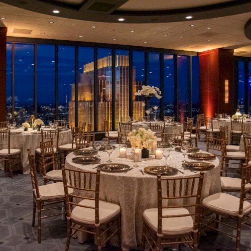 Elegant banquet hall at dusk with round tables, white linens, gold chairs, and floral centerpieces, ivy-lit windows, and warm ambient lighting.