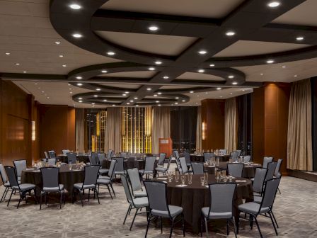 A spacious conference room set for a formal event with round tables, gray chairs, and soft lighting in a modern venue.